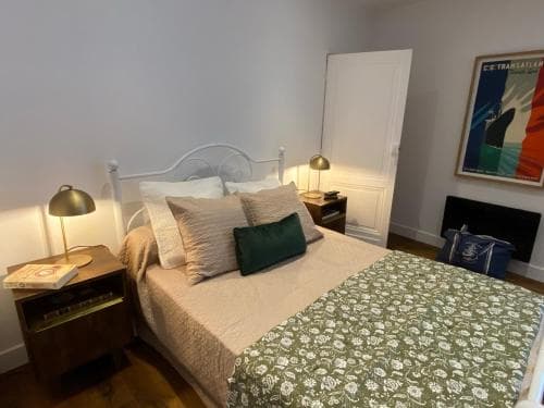 A cozy bedroom with a neatly made bed adorned with patterned bedding, vintage lamps on wooden nightstands, and a vibrant wall art piece, ideal for travelers seeking a comfortable and stylish accommodation.