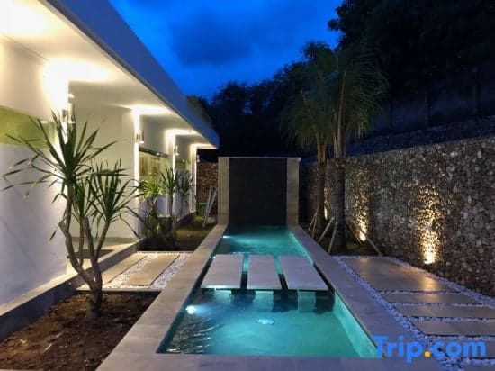 A serene evening scene showcases a modern villa's private pool area with floating loungers, illuminated pathways, lush tropical plants, and a stone wall backdrop, ideal for travelers seeking a tranquil retreat.