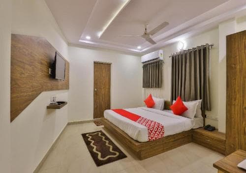 A cozy hotel room features a neatly made bed with red accents, wooden furnishings, and soft lighting, creating a welcoming atmosphere ideal for travelers seeking comfort and relaxation.