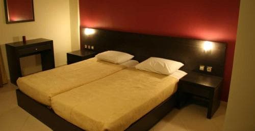 A cozy hotel room features a neatly made double bed with yellow linens against a warm red wall, accompanied by bedside tables and ambient lighting, ideal for travelers seeking comfort and relaxation.
