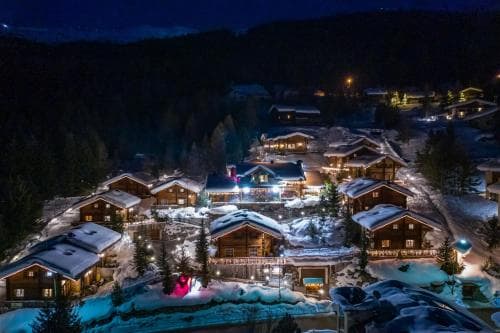 A cozy ski resort village glows warmly under the night sky, surrounded by snow-covered chalets and festive lights, ideal for winter getaways and family vacations.