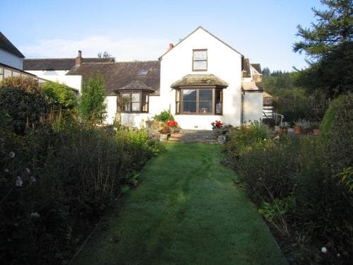 A serene countryside cottage with a lush garden pathway invites travelers seeking a peaceful retreat in a quaint village setting.