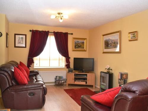 A cozy living room with leather sofas, red cushions, a wooden TV stand, and framed artwork creates a warm and inviting atmosphere, ideal for travelers seeking a comfortable stay in a homey vacation rental.