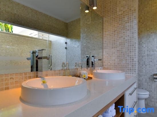 A modern bathroom with mosaic-tiled walls, dual sinks, and a large mirror offers a serene and luxurious ambiance, ideal for travelers seeking comfort in upscale accommodations.