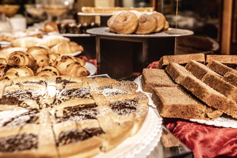 A cozy bakery display features an inviting array of pastries, including powdered donuts, chocolate-filled rolls, and layered cakes, perfect for a delightful culinary adventure.