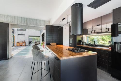 A sleek modern kitchen with black cabinetry, a wooden countertop island, and large windows inviting natural light creates an inviting atmosphere ideal for culinary enthusiasts seeking a stylish retreat.