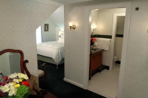 A cozy hotel room with a neatly made bed, a bathroom featuring a vanity and toilet, and a welcoming floral arrangement creates an inviting atmosphere ideal for travelers seeking comfort and relaxation.