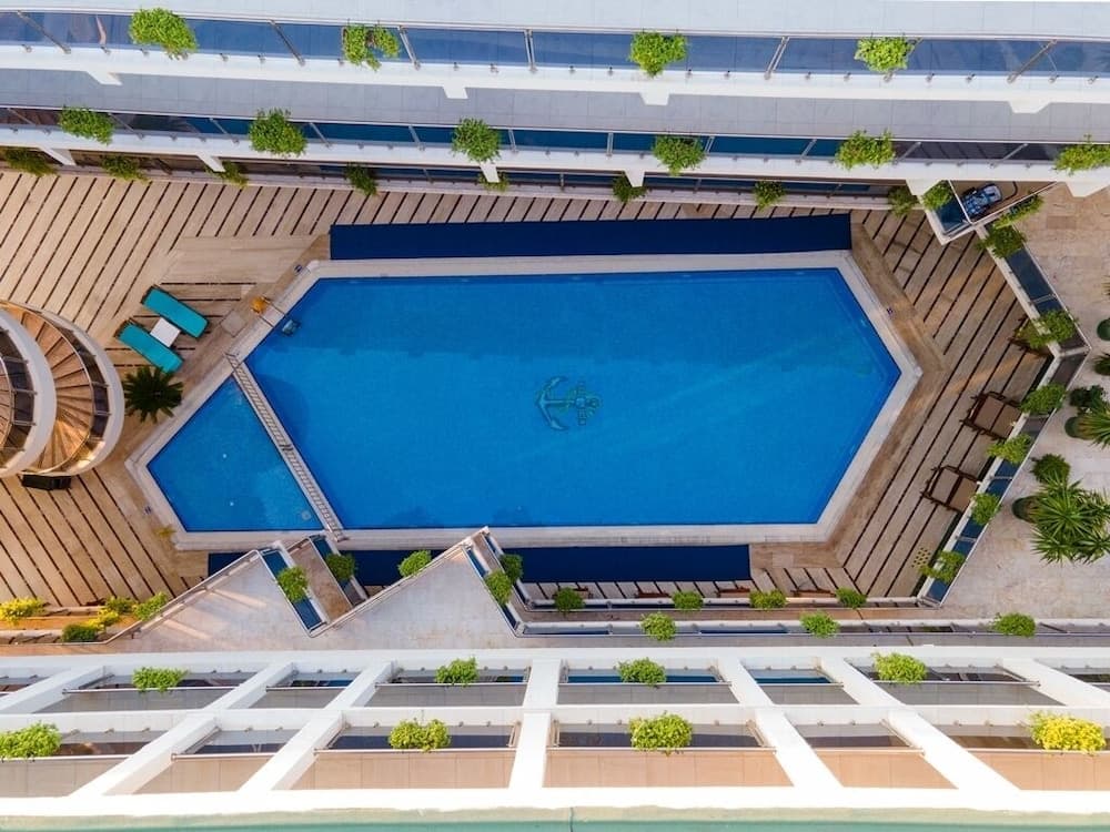 An aerial view of a serene rooftop pool surrounded by lush greenery and modern architecture, ideal for travelers seeking relaxation and luxury in an urban retreat.
