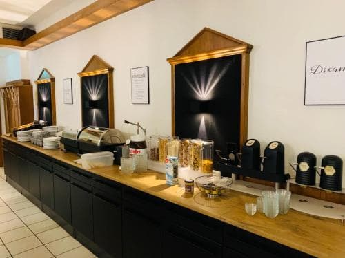 A cozy hotel breakfast area features a wooden counter lined with coffee dispensers, glassware, and neatly arranged pastries, creating an inviting atmosphere for travelers seeking a convenient morning meal.