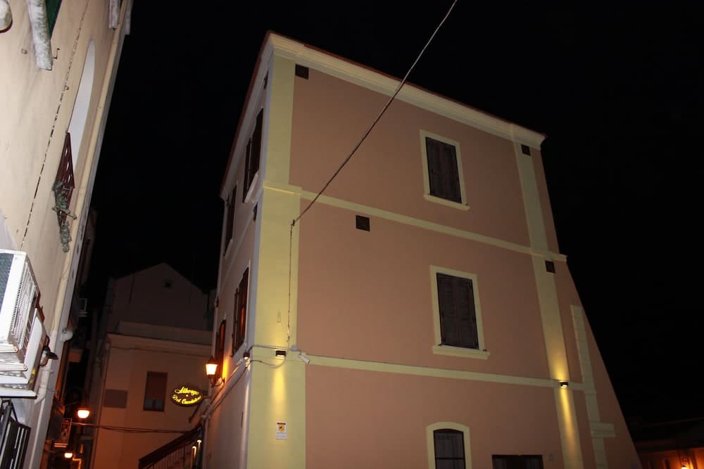 A cozy evening scene in an urban alleyway illuminated by warm streetlights, featuring pastel-colored buildings with wooden shutters, ideal for travelers exploring nightlife or seeking charming accommodations.