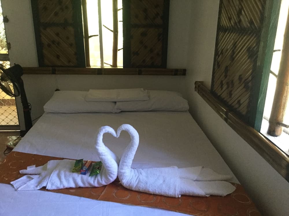 A cozy hotel room with bamboo accents features a neatly made bed adorned with towel swans forming a heart, creating a romantic and inviting atmosphere ideal for travelers seeking relaxation.