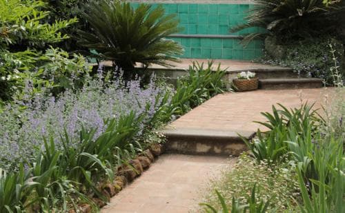 A serene garden path lined with vibrant greenery and blooming flowers leads to a tranquil poolside area, ideal for relaxation and nature photography.