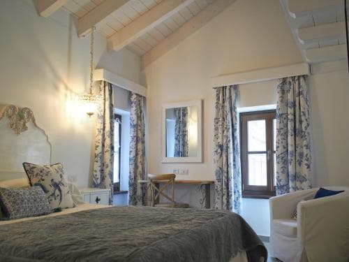 A cozy attic bedroom with sloped ceilings, blue-patterned curtains, and soft lighting creates a serene retreat, ideal for travelers seeking a charming and peaceful accommodation experience.