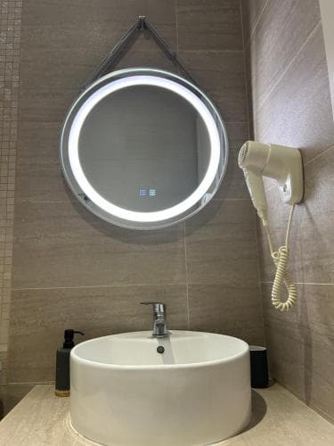 A modern bathroom features a sleek round sink, an illuminated mirror with touch controls, and a wall-mounted hairdryer, creating a clean and functional space ideal for travelers seeking comfort and convenience.