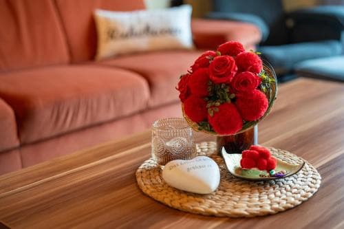 A cozy living room scene features a vibrant bouquet of red roses on a woven placemat alongside decorative items, evoking warmth and comfort ideal for a relaxing getaway or home tour photography.