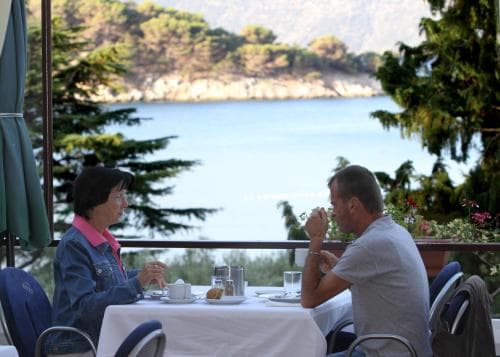 A serene lakeside café scene captures two individuals enjoying a meal amidst lush greenery and calm waters, ideal for travelers seeking a peaceful dining experience in nature.