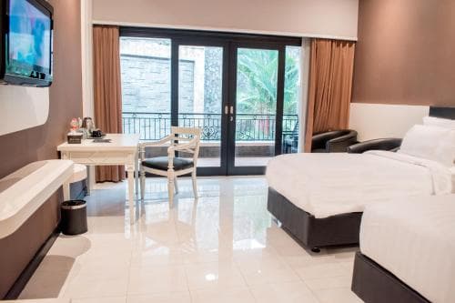 A modern hotel suite features a cozy bed, sleek desk area, bathtub, and balcony with lush greenery views, ideal for travelers seeking comfort and relaxation.
