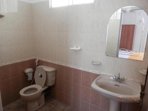 A clean, tiled bathroom with a toilet, sink, mirror, and towel rack offers a functional space for travelers seeking basic amenities in accommodations.