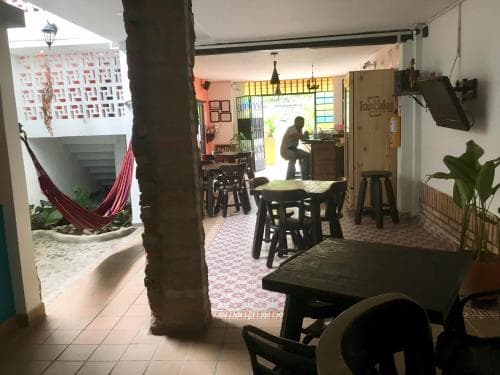 A cozy indoor-outdoor café with tiled floors, wooden tables, a hammock, and potted plants offers a relaxed atmosphere ideal for travelers seeking a tranquil spot to unwind and enjoy local culture.