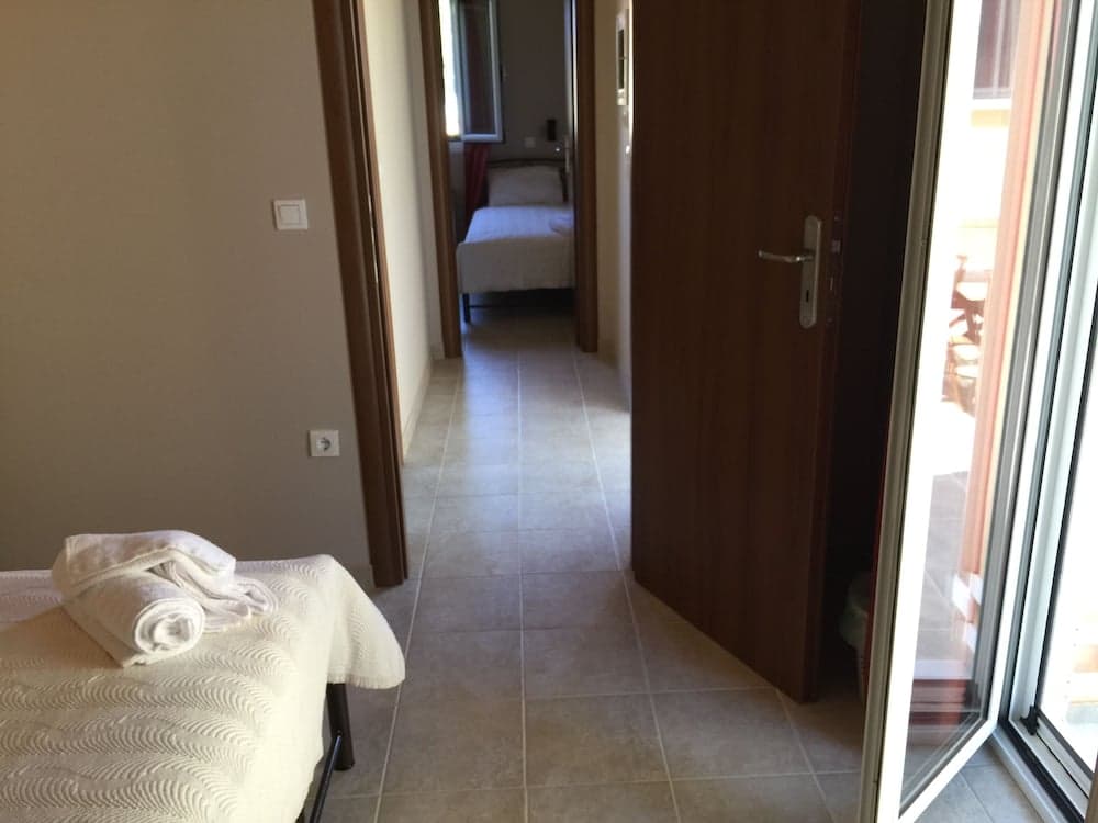 A cozy hotel room hallway with tiled floors, a neatly folded towel on a bed, and a bright balcony entrance, ideal for travelers seeking comfort and relaxation.