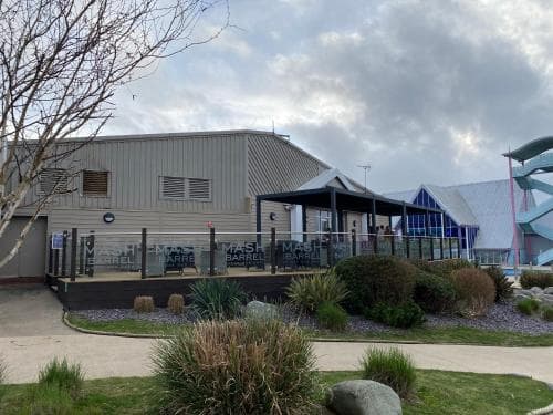 A serene outdoor scene featuring a modern building with a covered patio area, surrounded by lush greenery under a cloudy sky, ideal for travelers seeking a peaceful retreat or a family-friendly destination with nearby amenities.