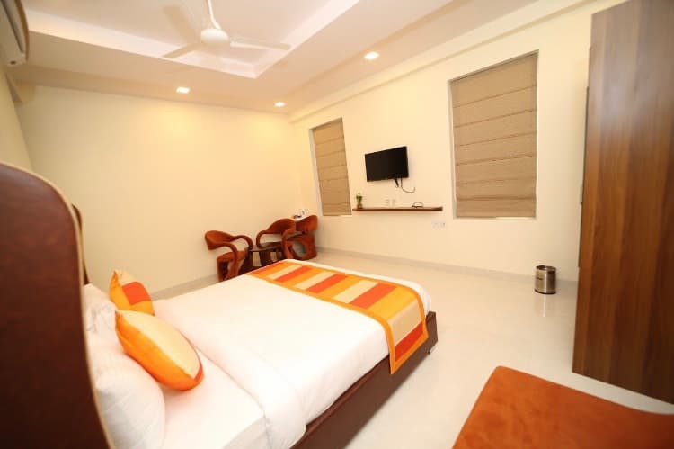 A cozy hotel room in Jaipur, Rajasthan, features a neatly made bed with orange accents, a wall-mounted TV, and modern furnishings, ideal for travelers seeking comfort and convenience.