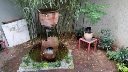 A serene courtyard garden features a tiered water fountain surrounded by bamboo plants, small tables with decorative pots, and a tranquil atmosphere ideal for relaxation and meditation.