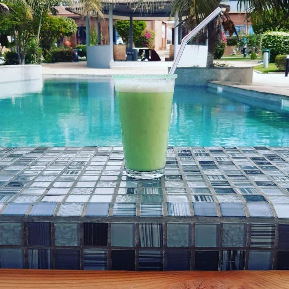 A refreshing green drink sits on a tiled ledge by a serene poolside, surrounded by lush tropical foliage, ideal for a relaxing vacation getaway.
