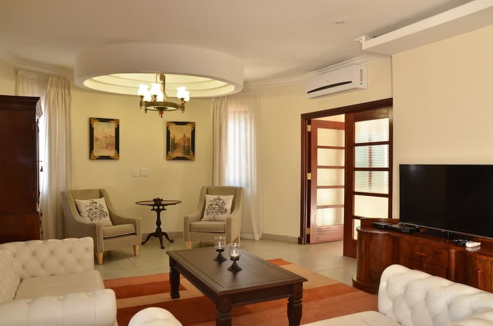 A cozy living room with beige walls, elegant furniture, framed artwork, and soft lighting creates a serene atmosphere ideal for travelers seeking comfort in a vacation rental.