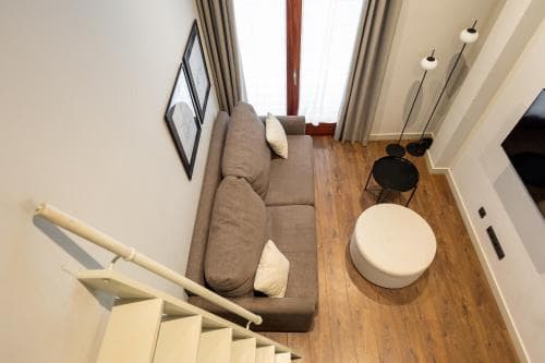 A cozy modern living room with a plush sofa, wooden flooring, and a staircase leading up, ideal for travelers seeking a stylish and comfortable apartment stay.