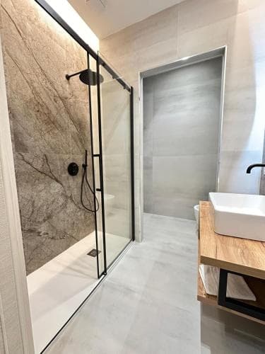 A modern bathroom features a sleek glass-enclosed shower with a marble accent wall, a minimalist sink on a wooden vanity, and a clean, contemporary design ideal for travelers seeking upscale accommodations.