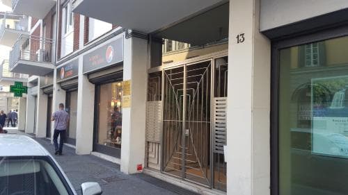 A bustling urban street scene features a closed storefront with metal gates, a pharmacy sign, pedestrians, and parked cars, ideal for city exploration and local shopping experiences.