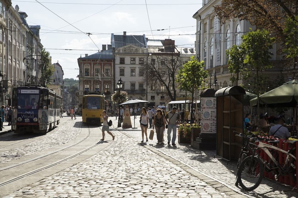 A lively cobblestone street in a historic European city features trams, pedestrians, and charming cafes, ideal for urban exploration and cultural immersion.