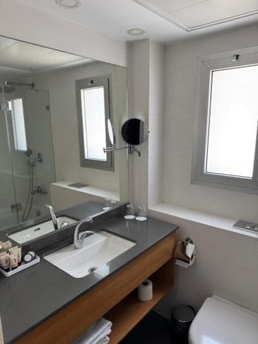 A modern hotel bathroom features a sleek double sink vanity, large mirror, and natural light from a window, creating a clean and inviting atmosphere ideal for travelers seeking comfort and functionality.