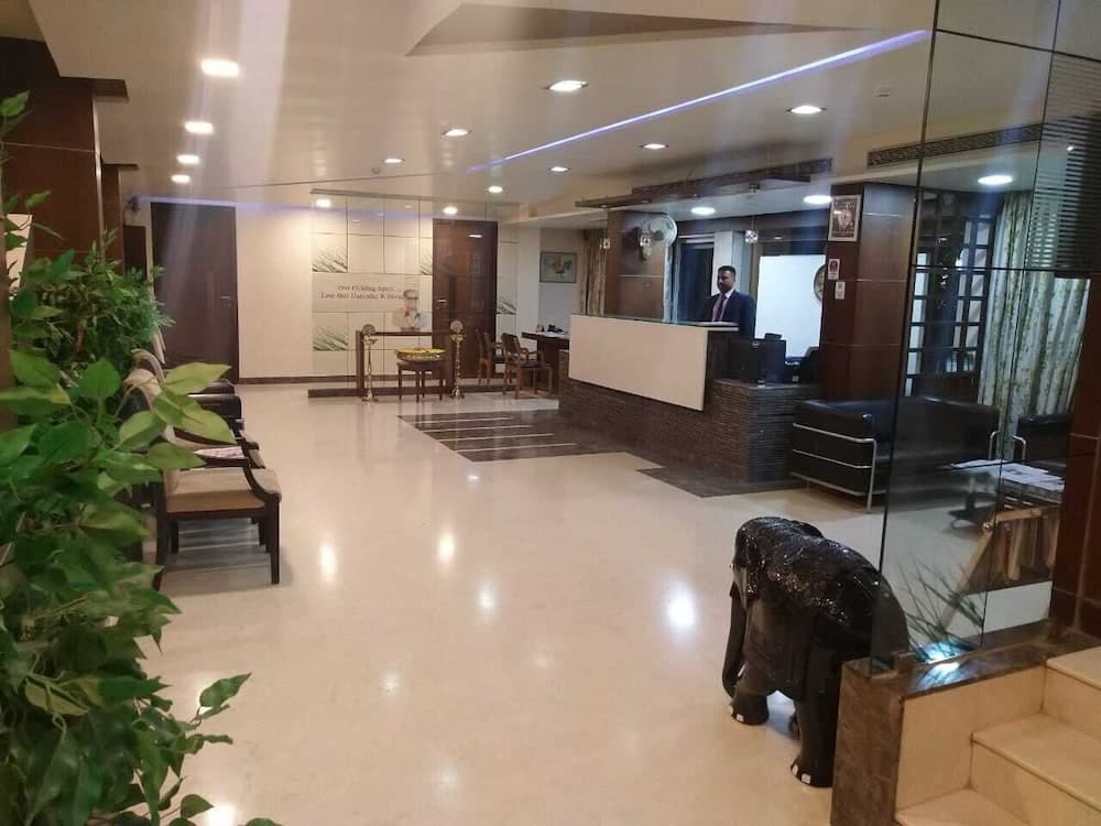 A modern hotel lobby features a sleek reception desk, plush seating areas, vibrant greenery, and an elephant statue, creating a welcoming atmosphere ideal for travelers seeking comfort and convenience.