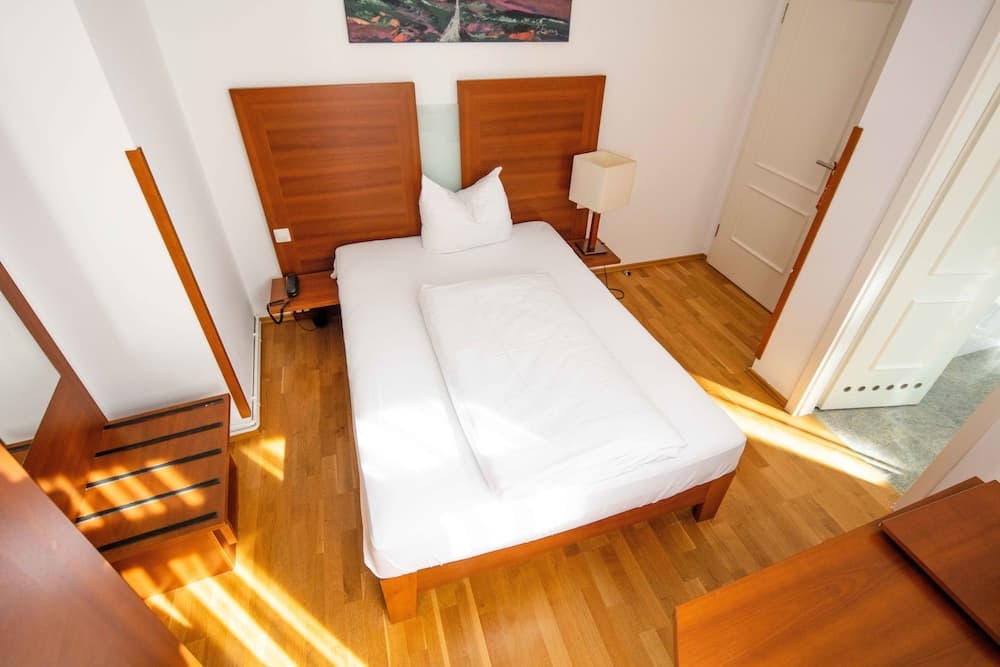 A cozy loft bedroom with wooden floors, a neatly made bed, and warm sunlight streaming in, ideal for travelers seeking a serene and stylish accommodation experience.