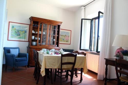A cozy dining room with terracotta flooring, wooden furniture, and a sunlit window creates an inviting atmosphere, perfect for travelers seeking a warm and homely accommodation experience.
