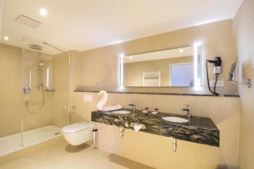 A modern hotel bathroom features a sleek glass shower, a floating marble vanity with dual sinks, and a cozy ambiance enhanced by soft lighting, ideal for travelers seeking comfort and luxury.