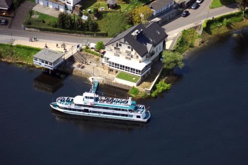 An aerial view captures a serene riverside town with a bustling ferry docked near quaint houses, ideal for travelers seeking a peaceful river cruise experience.