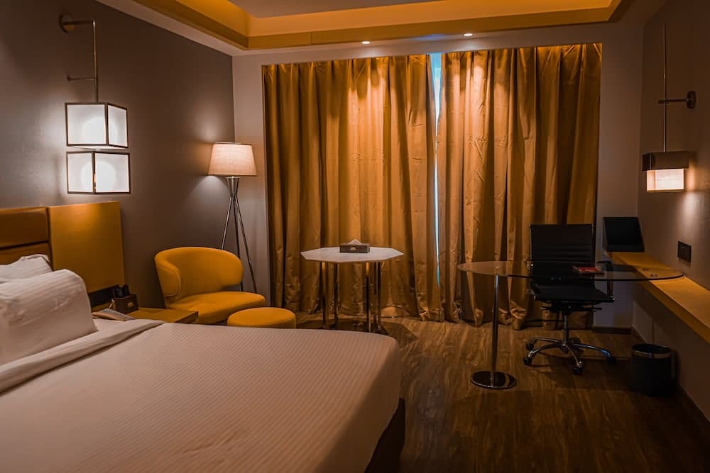 A cozy hotel room with warm lighting, yellow curtains, modern furniture, and a serene ambiance is ideal for travelers seeking comfort and relaxation during their stay.