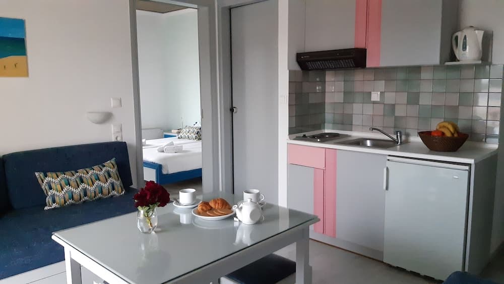 A cozy studio apartment features a modern kitchenette with pink accents, a dining area set for breakfast, and a glimpse of a bedroom, ideal for a comfortable solo traveler's retreat.