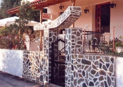 A charming villa entrance with stone walls and a black gate invites travelers to explore its serene garden setting, perfect for a relaxing getaway.