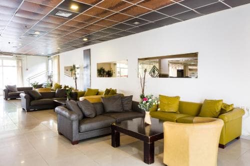 A modern hotel lobby features sleek sofas in gray and yellow, a polished floor, and decorative mirrors, creating a welcoming atmosphere ideal for travelers seeking comfort and style.
