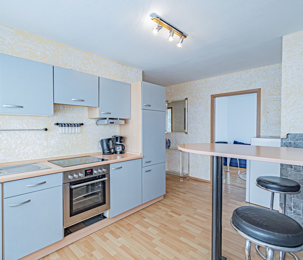 A cozy kitchen with light blue cabinets, wooden flooring, and a bar counter with stools offers a welcoming space for travelers seeking a homey cooking experience in their vacation rental.