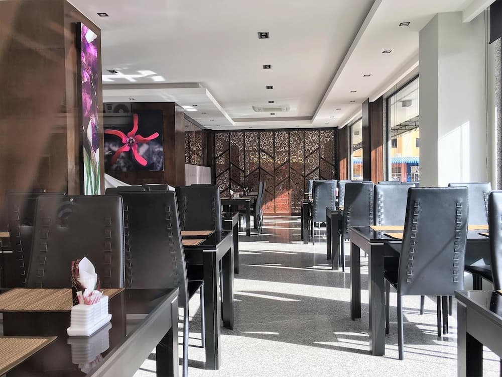 A modern restaurant interior features sleek black tables and chairs under bright sunlight streaming through large windows, creating an inviting atmosphere ideal for travelers seeking a stylish dining experience.