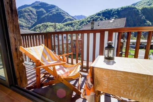 A cozy balcony with wooden furniture and a scenic mountain backdrop offers a serene retreat for travelers seeking relaxation in a picturesque alpine setting.
