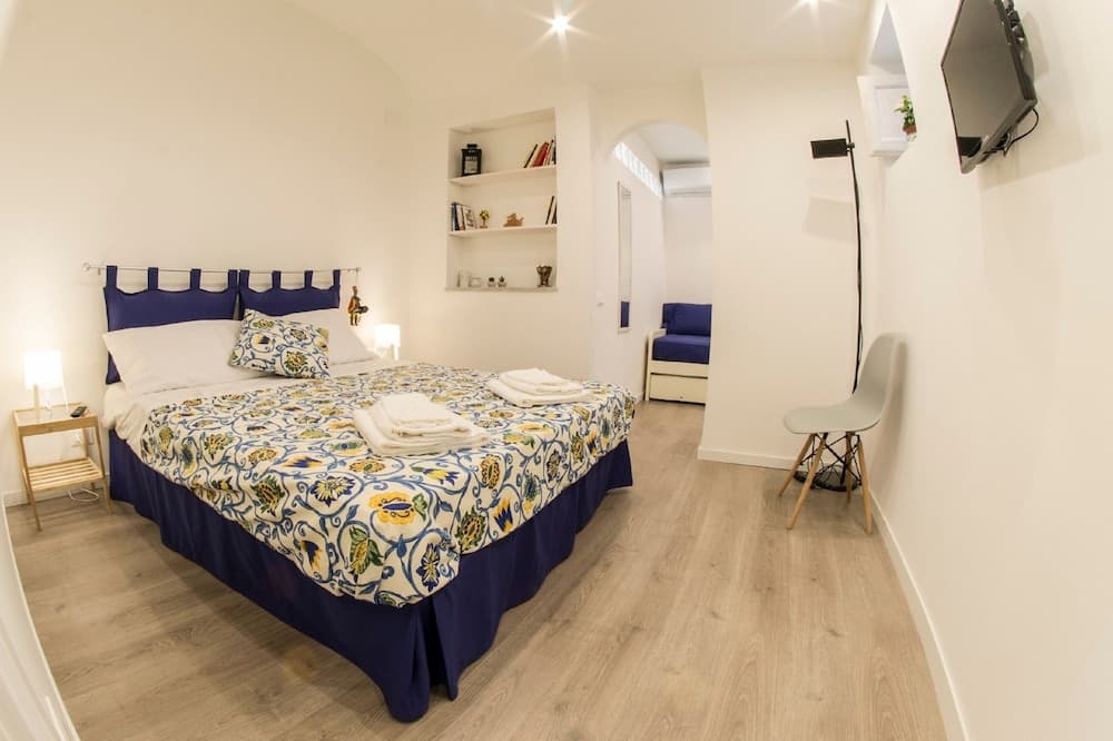 A cozy bedroom with a vibrant floral bedspread, wooden flooring, and modern furnishings creates an inviting atmosphere ideal for travelers seeking comfort in a boutique hotel setting.