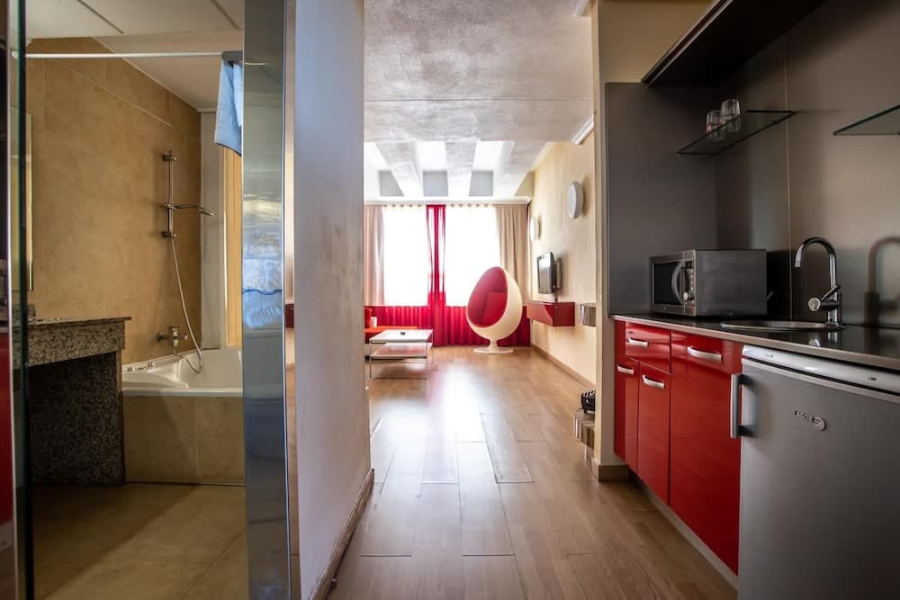 A cozy apartment features a modern kitchen with red cabinets, a stylish living area with a unique egg-shaped chair, and a well-lit bathroom, ideal for travelers seeking comfort and functionality in urban accommodations.