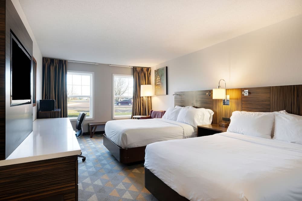 A cozy hotel room with two neatly made beds, a desk with a chair, and large windows letting in natural light, ideal for travelers seeking comfort and convenience during their stay.