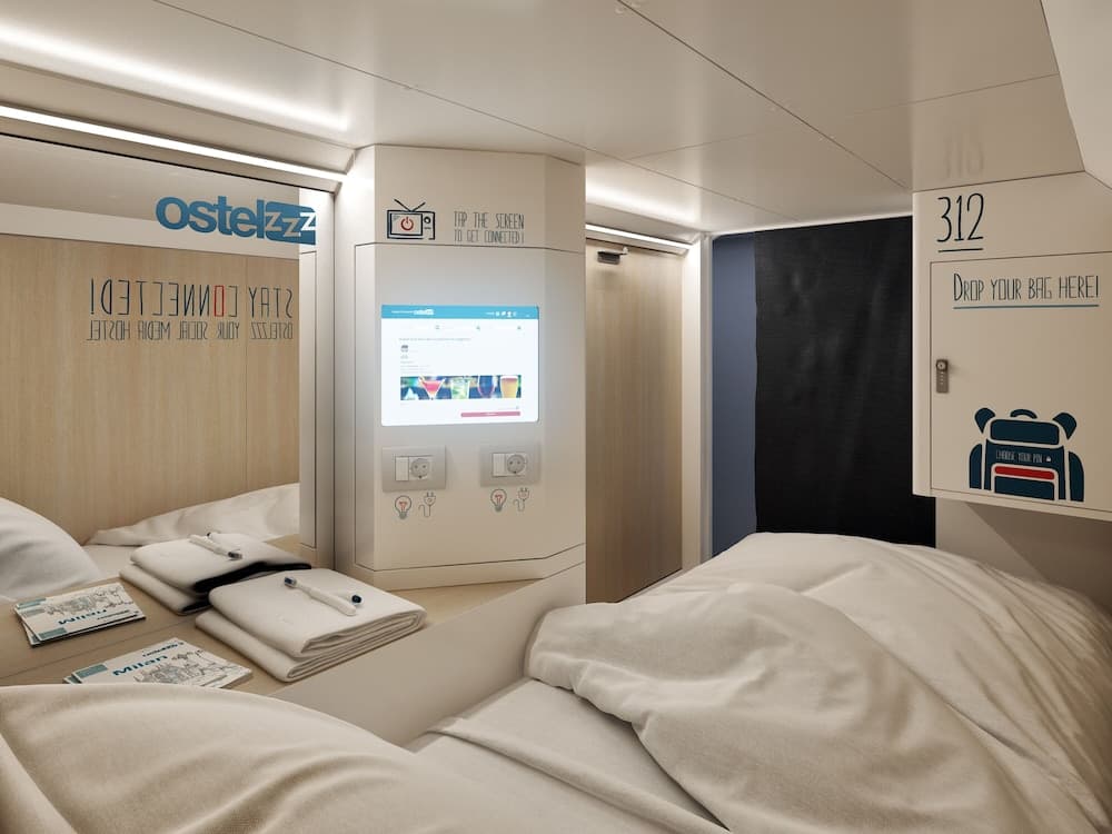 A cozy, modern hostel room features sleek beds, a touchscreen entertainment system, and minimalist decor, ideal for budget travelers seeking comfort and connectivity.
